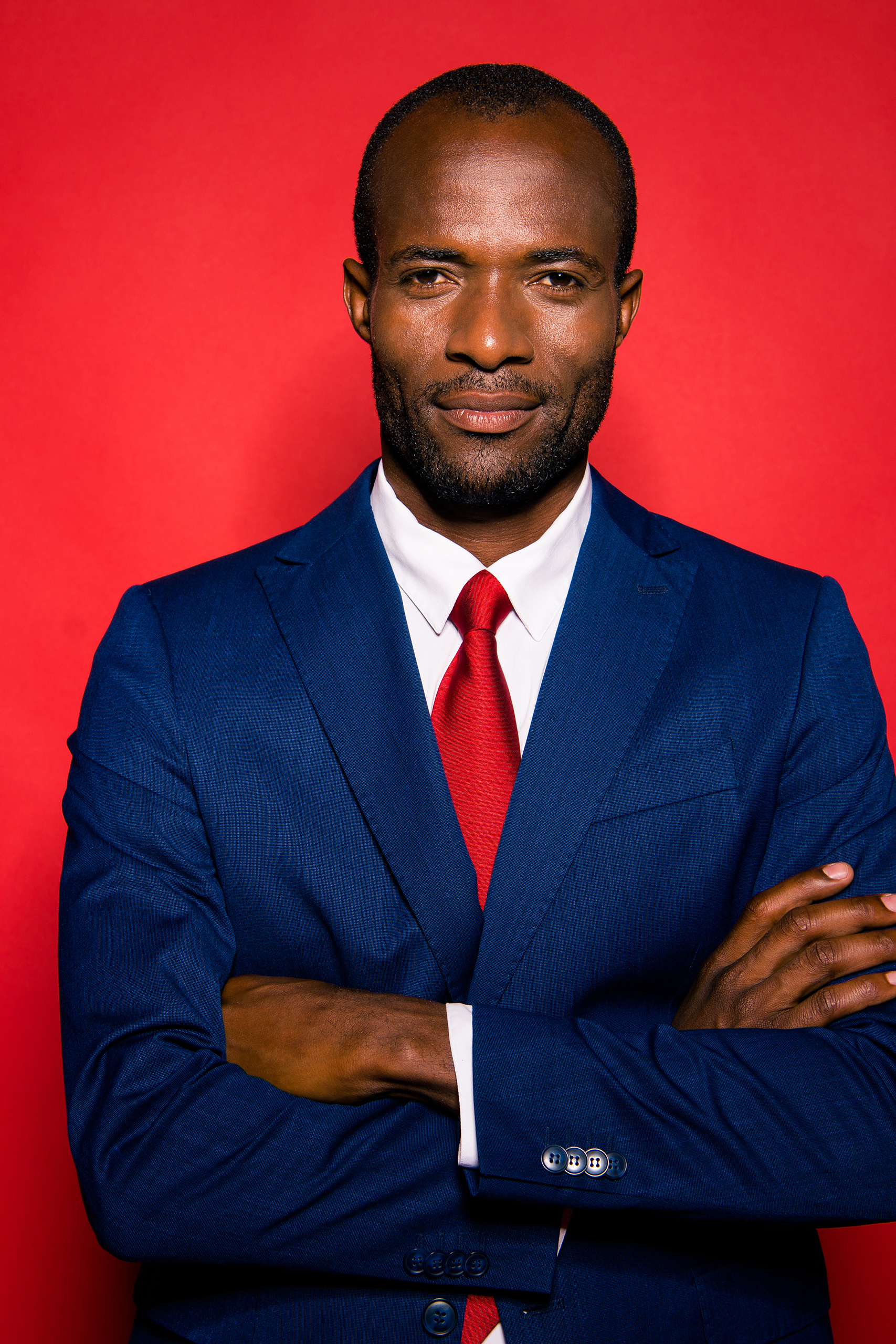 Professionnel en costume bleu avec une cravate rouge, debout avec les bras croisés devant un fond rouge, illustrant la confiance et l'expertise dans le domaine juridique. Cette image symbolise l'approche stratégique et personnalisée de Madagasy.com pour les professionnels du droit, mettant en avant l'importance de la gestion digitale et du référencement SEO pour une visibilité optimale sur le web.