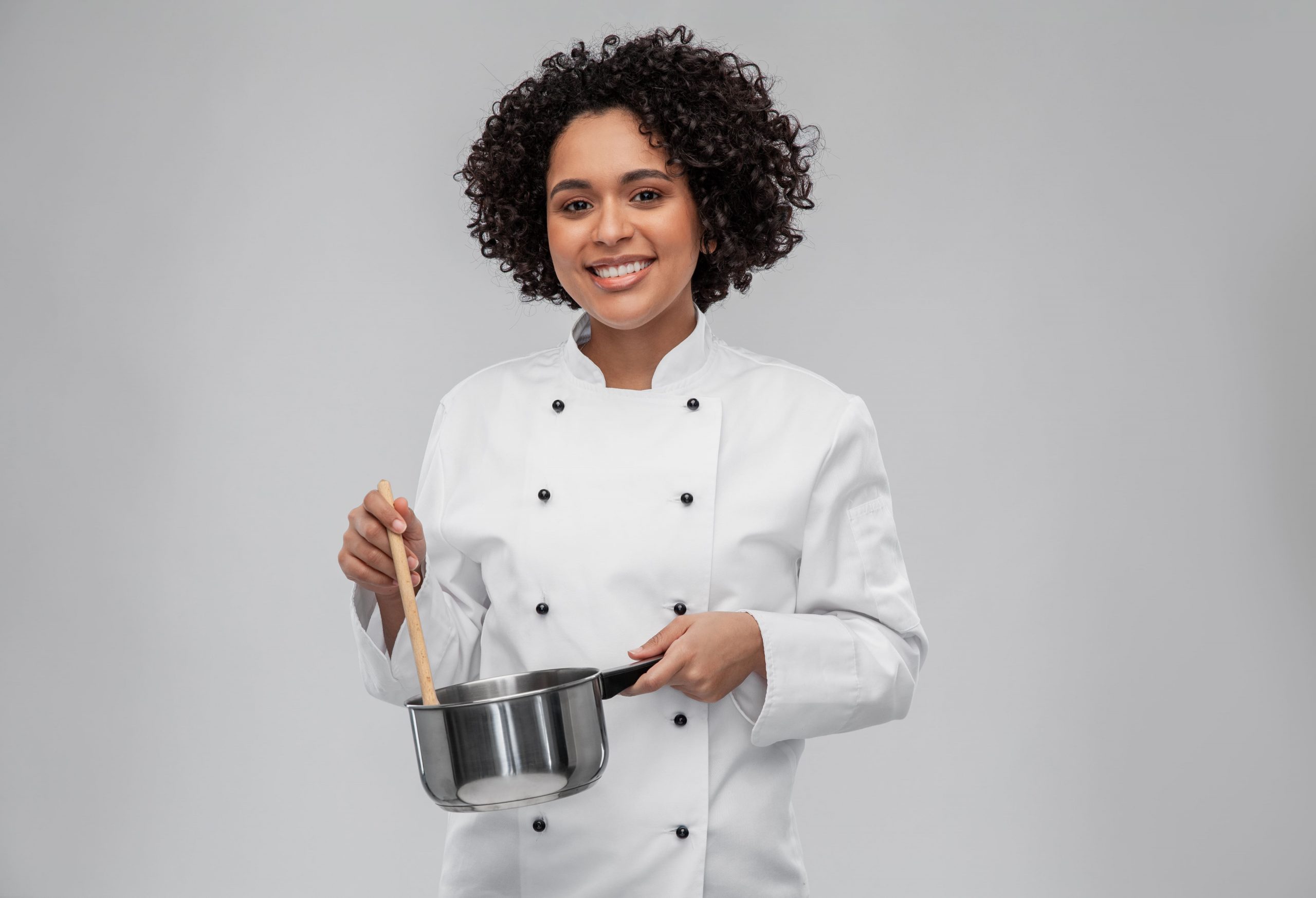 Chef cuisinier en uniforme blanc, remuant un plat dans une casserole en acier inoxydable, illustrant le savoir-faire et la passion des meilleurs chef à domicile Madagascar.