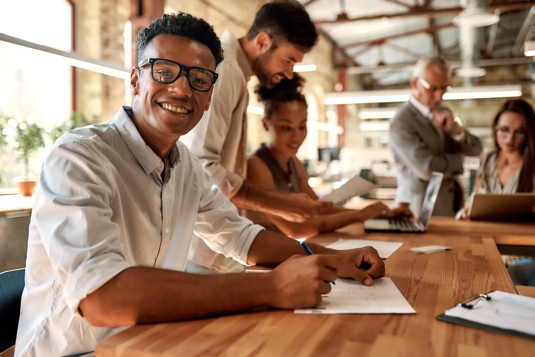 Un groupe de personnes collaborant dans un bureau moderne avec lumière naturelle et un décor industriel, représentant le travail d'équipe et l'innovation, promus par Madagasy.com pour inspirer le développement professionnel à Madagascar.